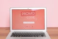 Laptop with activated promo code on wooden table near pink wall