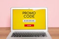 Laptop with activated promo code on wooden table near pink wall