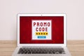 Laptop with activated promo code on wooden table near white wall