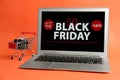 Laptop with Black Friday announcement, small shopping cart and gift on orange background Royalty Free Stock Photo