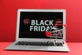 Laptop with Black Friday announcement, small shopping cart and gift on red background Royalty Free Stock Photo