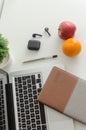 Laptop, black wireless earbuds, notebook, pen, potted plant, apple and orange on white background Royalty Free Stock Photo