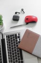 Laptop, black wireless earbuds with a red mouse, notebook, pen, potted plant on white background