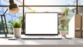 A laptop with a blank frameless screen mockup template is positioned on a table in an office interior, offering a front view, with