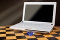 Laptop with blank screen and dices on wooden chessboard