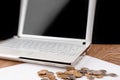 Laptop with blank screen and heap of coins on wooden table