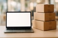 Laptop with a blank screen sits next to a stack of three cardboard boxes on a wooden table Royalty Free Stock Photo