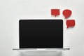 Laptop with blank screen on white background near empty red speech bubbles, cyberbullying concept.