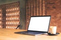 Laptop with blank white desktop screen and coffee cup on wooden table with brick wall background Royalty Free Stock Photo