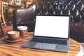 Laptop with blank white desktop screen and coffee cup on wooden table in cafe