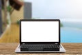 Laptop with blank white screen on vintage wooden table on blurred pool and beach background Royalty Free Stock Photo