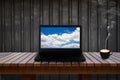 Laptop with blue sky and cloud on screen on wooden table and a cup of coffee. Royalty Free Stock Photo