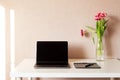 Laptop, bouquet of tulips and graphics tablet on white table.