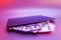 Laptop with bundles of dollars and euros against a background of colorful bright neon UV blue and purple lights Royalty Free Stock Photo