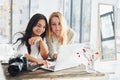 With laptop and camera. Two young female freelancers working indoors in the office at daytime