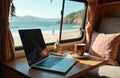Laptop on camper van table with coffee cup, notebook. Beach with ocean, mountain in background. Alternative office for remote Royalty Free Stock Photo