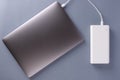Laptop charging with power bank by white USB cable. Modern external portable charger