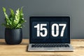 Laptop with clock screensaver placed on wooden desk with fresh green potted plant