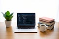 Laptop with code on screen, stack of books, coffee mug, and plant on wooden desk, home office setup Royalty Free Stock Photo