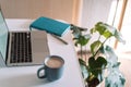 Laptop with coffee cup on desktop with notepad and home plants