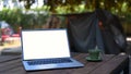 Laptop computer with blank screen and coffee cup on wood table near camping tent. Royalty Free Stock Photo