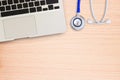 Laptop computer with blue stethoscope on wooden desk. Royalty Free Stock Photo