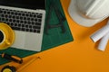 Laptop computer, blueprints, safety hardhat, coffee cup and stationery on yellow background