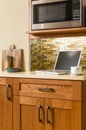 Laptop computer and coffee cup on counter in contemporary home kitchen with wood cabinets and glass tile backsplash Royalty Free Stock Photo