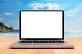 Laptop computer with empty blank white screen for copy space on wooden desk with blurry summer sea ocean beach at background.
