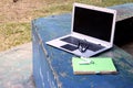 Laptop computer, eyeglasses, notebook and pen at an outdoor park