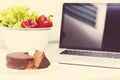 Laptop computer in kitchen with Veinna cake and colorful vegetables Royalty Free Stock Photo