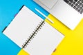 Laptop computer, open paper notebook and white pen on blue and yellow color background. Top view, copy space for text Royalty Free Stock Photo