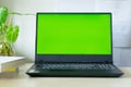 Laptop computer showing chroma green screen on LCD display stands on a desk with books next to ready for further design and copy Royalty Free Stock Photo