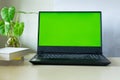 Laptop computer showing chroma green screen on LCD display stands on a desk with books next to ready for further design and copy Royalty Free Stock Photo