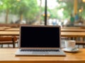 Laptop computer sits on a wooden table in a cafe