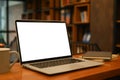 Laptop computer with white empty screen, coffee cup and supplies on wooden table in contemporary office Royalty Free Stock Photo