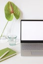 Laptop or computer with white screen on the white table with anthurium flower in vase. Home office workspace concept. Royalty Free Stock Photo