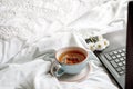 Laptop, a cup of tea,White bed and plaid. sunny morning and breakfast. work online in a comfortable home. cozy bright room Royalty Free Stock Photo