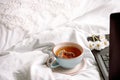 Laptop, a cup of tea,White bed and plaid. sunny morning and breakfast. work online in a comfortable home. cozy bright room Royalty Free Stock Photo