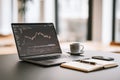 Laptop displaying financial data analysis with coffee cup and notebook on modern workspace Royalty Free Stock Photo