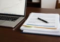 Laptop displaying a line graph sits beside a stack of documents on Royalty Free Stock Photo