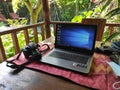 a laptop and DSLR camera on a wooden table covered with red patterned cloth, with a wooden fence Royalty Free Stock Photo