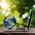 Laptop with earth globe on wooden table and green bokeh background