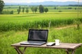 laptop and 3g router on a wooden bench amidst green fields