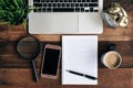 Laptop, green plant, clock, magnifying glass, phone, coffee and blank notebook on a wooden table