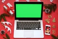 Laptop with green screen, mobile phone and Christmas decorations on red background.Concept: selection gifts, online shopping,