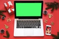 Laptop with green screen, mobile phone and Christmas decorations on red background.Concept: selection gifts, online shopping,