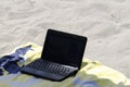 A laptop lays on towel in the beach