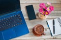 Laptop, notebook with pen, cup of coffee, smartphone and vase with flowers on your desktop
