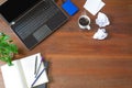 Laptop with office supplies, crumpled paper, green plant and hot black coffee with smoke on vintage grunge wooden desk background Royalty Free Stock Photo